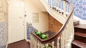 Eine Wendeltreppe mit weißen Balustraden und einem braunen Geländer, die zu einem Raum mit einer gefliesten Wand und einer Tür mit der Aufschrift 'Arménio' führt.