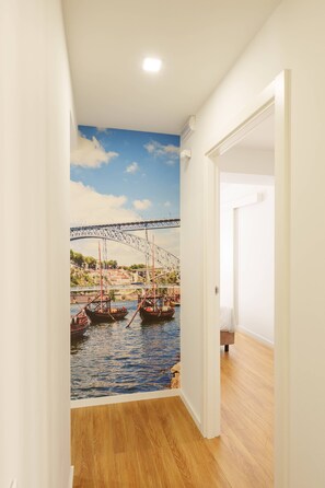 Ein Flur mit Wandgemälde einer Brücke über Wasser, Holzdielenboden und einer weißen Tür.