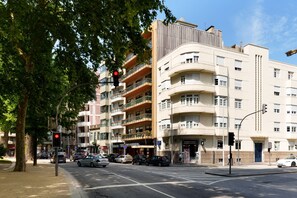 Ein mehrgeschossiges Gebäude mit Balkonen, eine Straßenscharte und Autos.