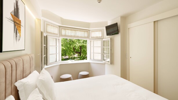 A bedroom with a large bed, a window with curtains, a television on the wall, and a radiator. - VIVA Casa da Música Apartment (Porto)