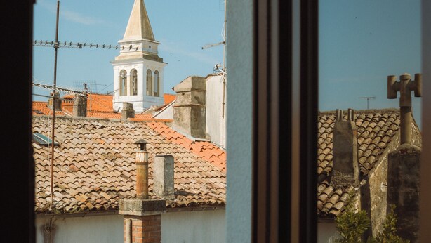 Vista de um edifício com uma torre, telhados de telhas vermelhas e céu claro.