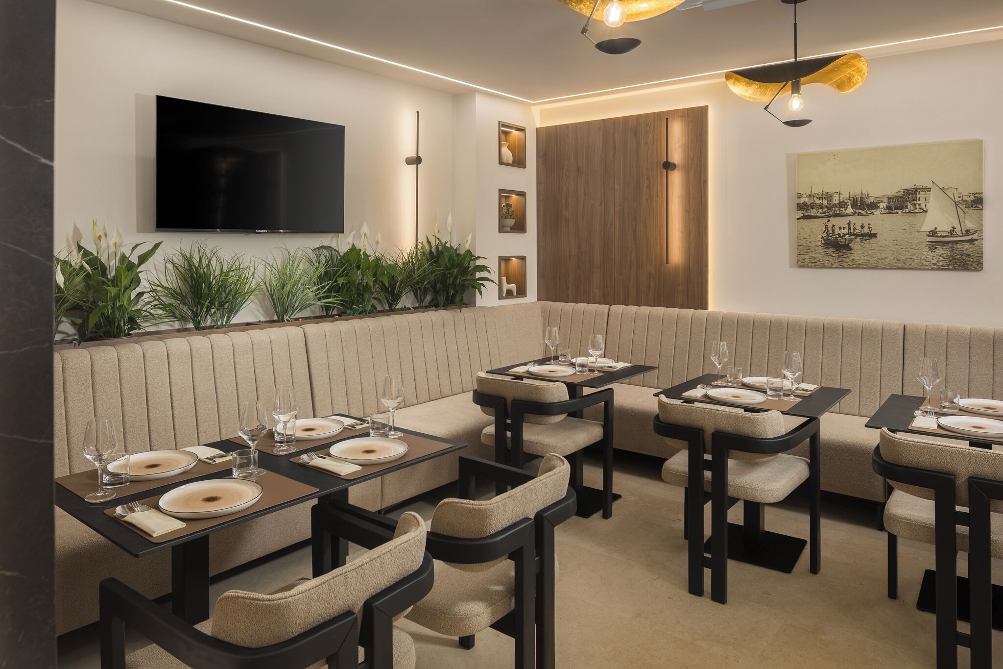 A restaurant with a TV mounted on the wall, a wooden panel wall, and a painting of a harbor.