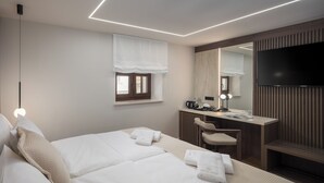 Habitación de hotel con dos camas, un escritorio, una silla, un televisor y una ventana con un dosel blanco.