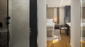 Quarto de hotel moderno com chuveiro, cama, escrivaninha e uma cadeira.