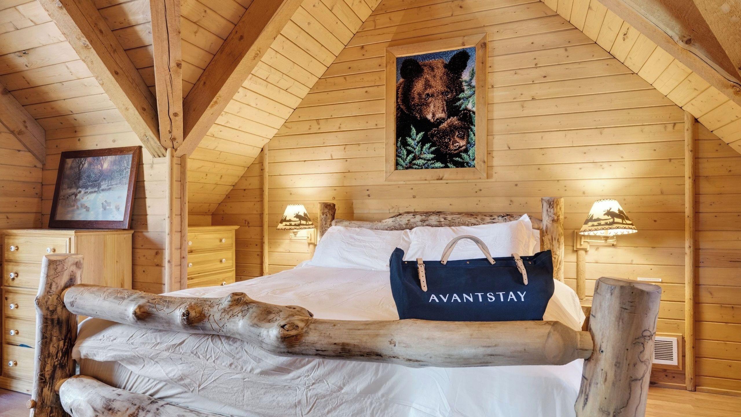 Ein Schlafzimmer einer Holzhütte mit einem Bett, einem Holz-Kopfteil, zwei Wandleuchten, einem gerahmten Bild und einem Nachttisch mit einer Lampe.