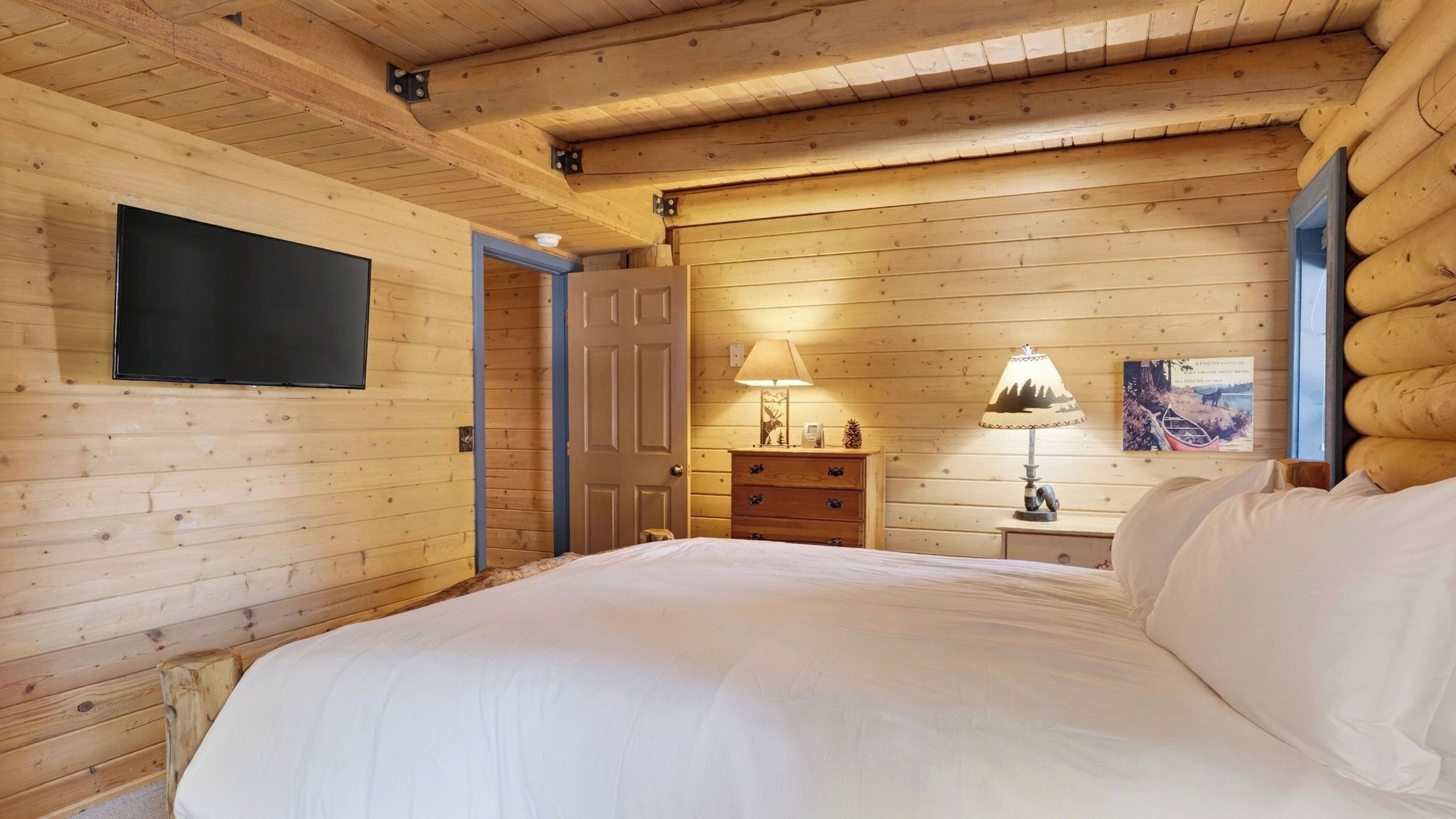 Camera da letto in una baita di legno con un letto, una cassettiera, una lampada e un televisore montato a parete.