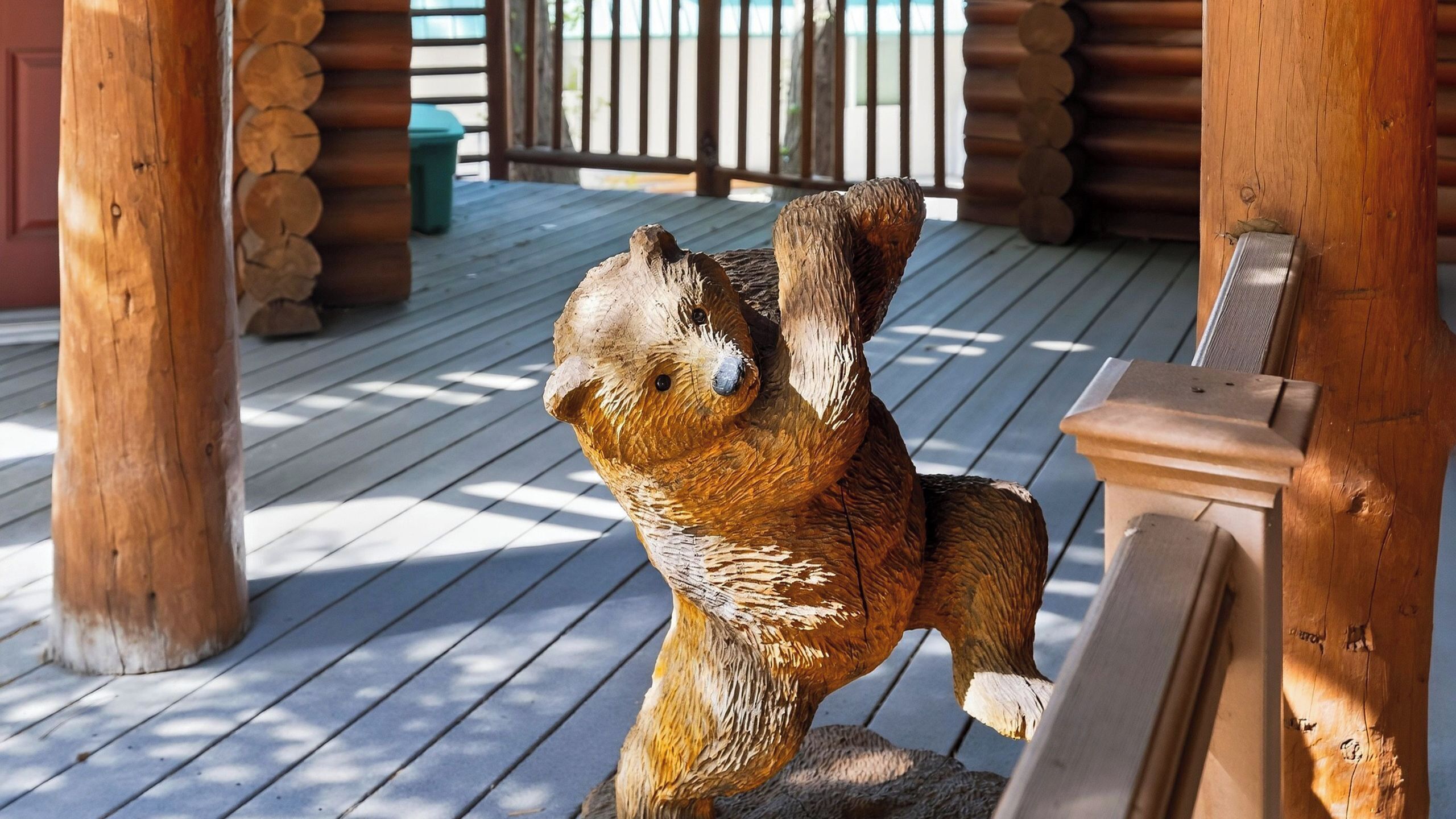 A wooden bear sculpture on a wooden deck with a wooden fence in the background.