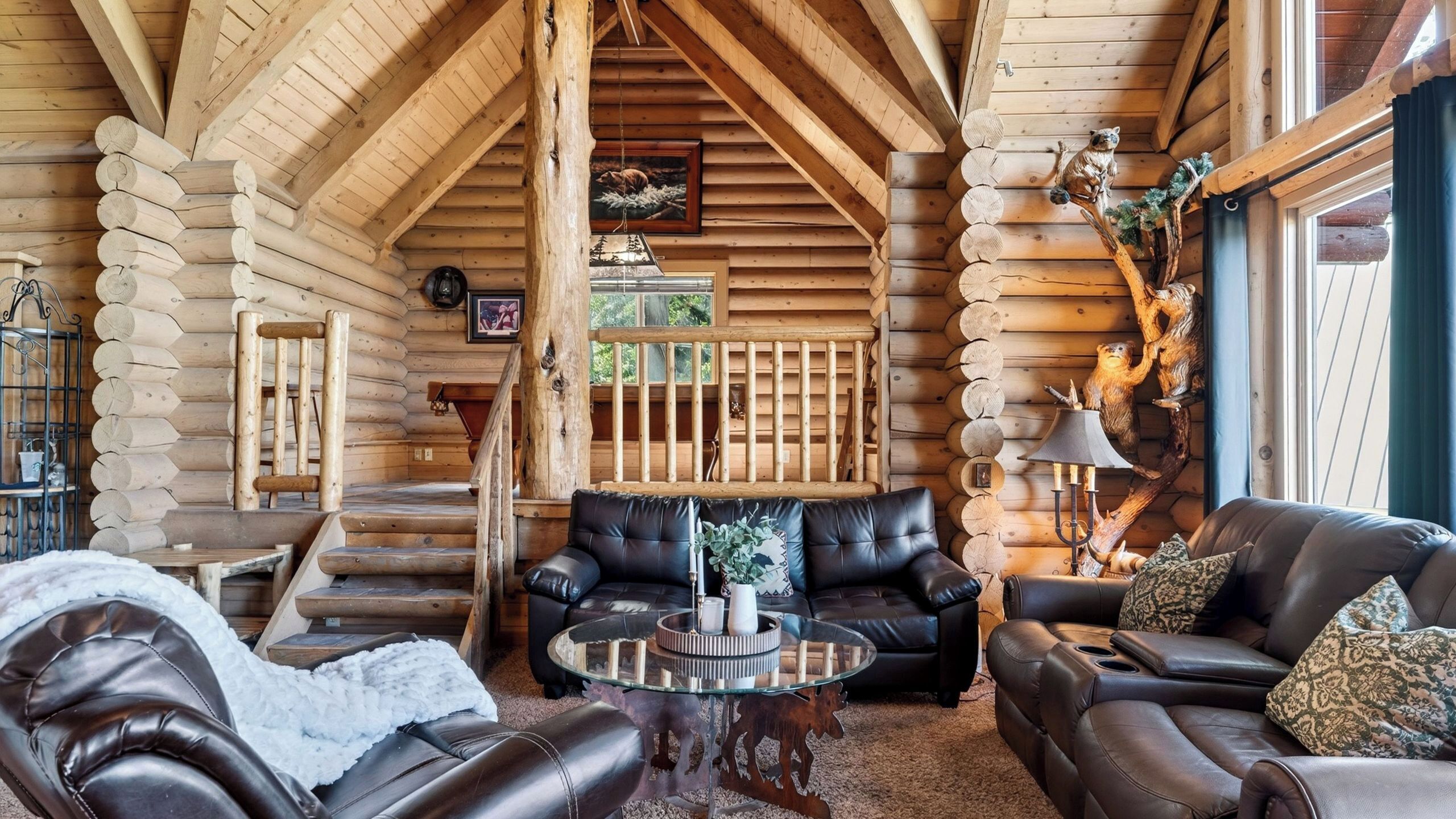 A log cabin interior with leather furniture, a glass coffee table, and a fireplace.