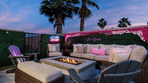 An outdoor patio with a fire pit, wicker furniture, and a wall decorated with flowers. - La Casita Retreat Coachella by Avantstay Pool + Spa Desert Home + Putting Green + Game Room (Coachella)