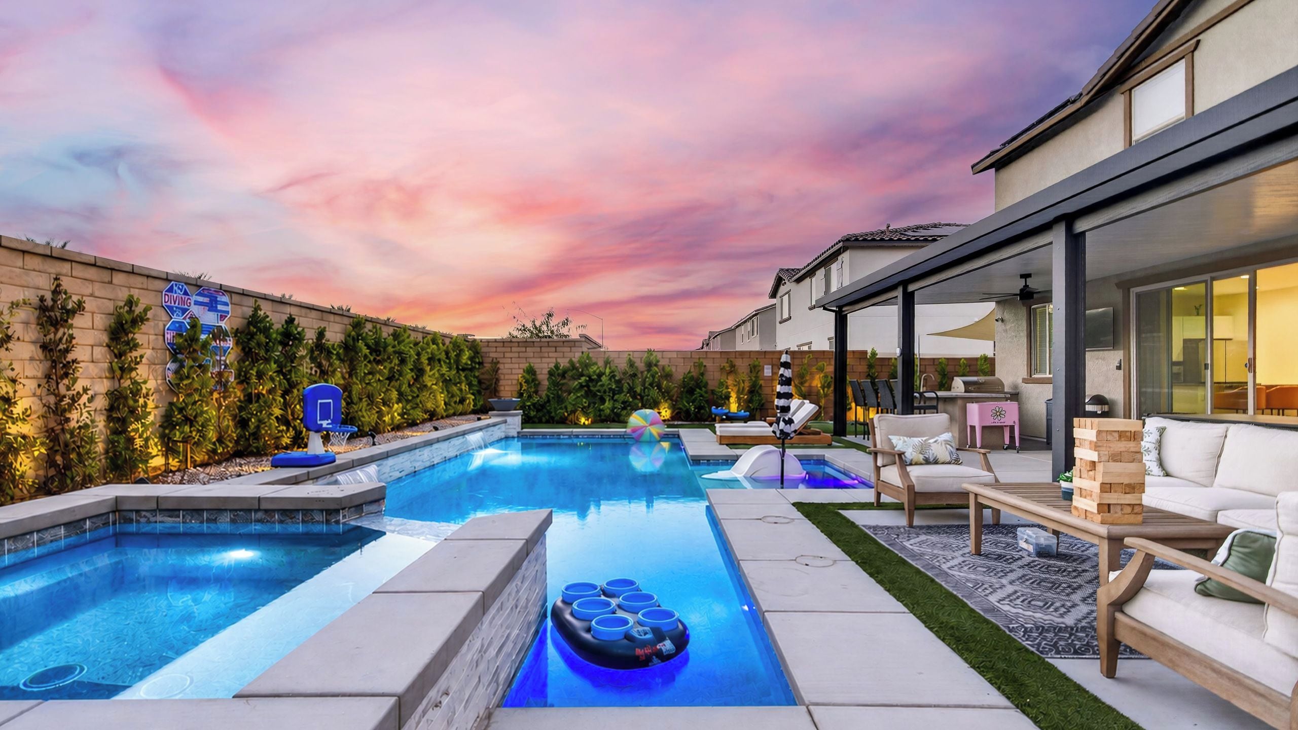 A modern outdoor pool area with a sunset view, a covered seating area, and a barbecue setup.