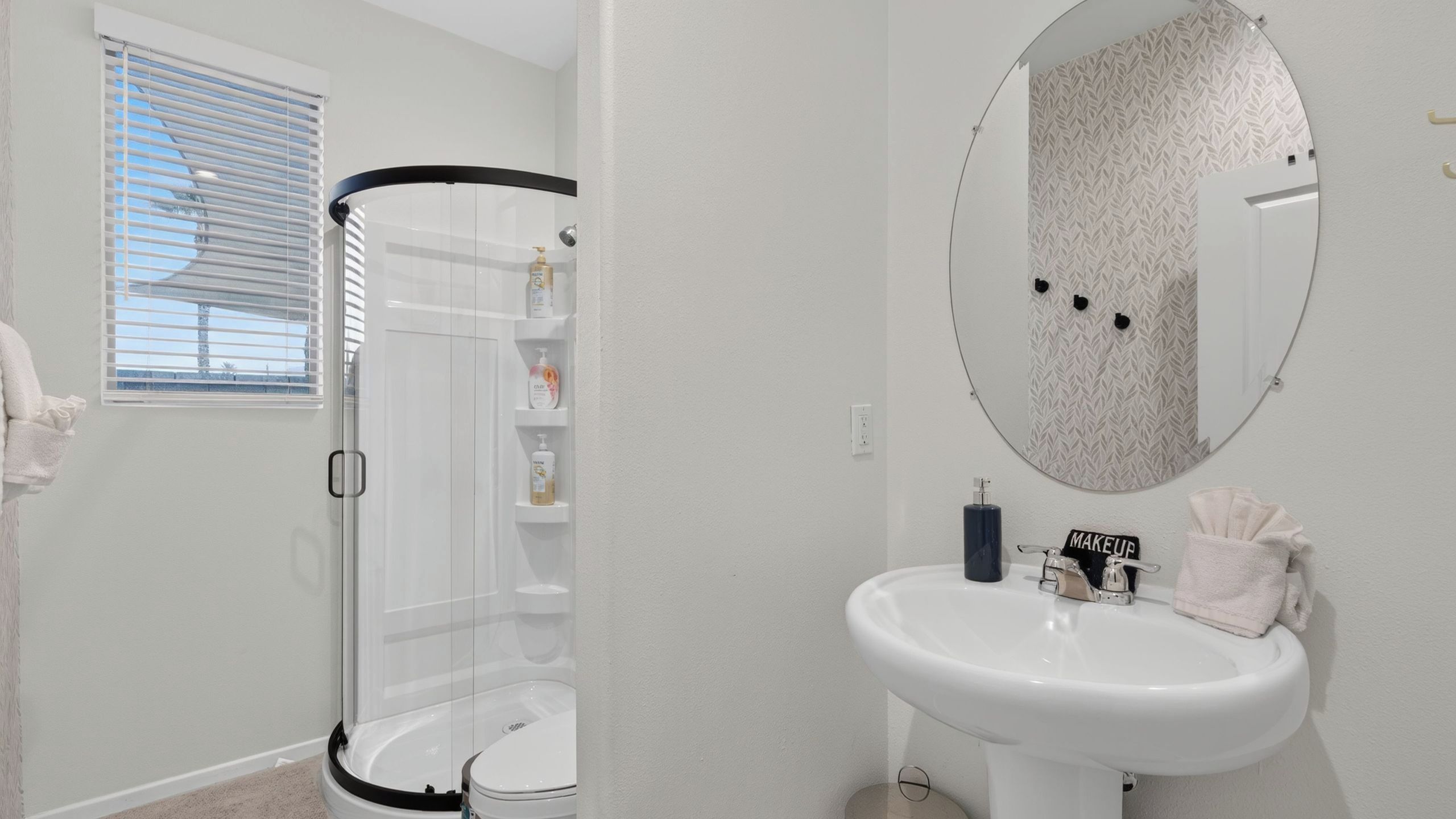 Un baño con cabina de ducha, lavamanos, espejo y toallero.