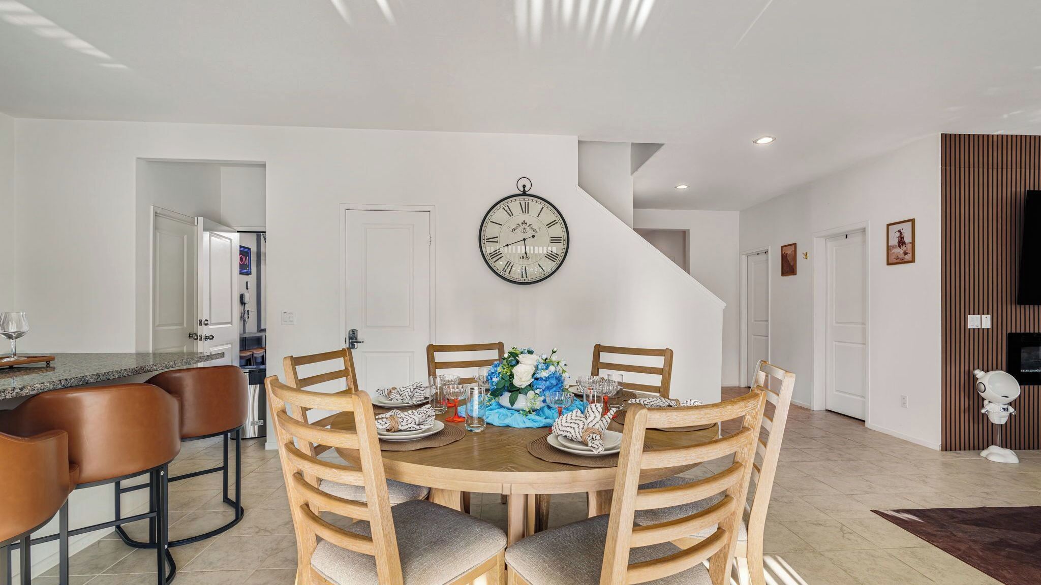 Un comedor con una mesa redonda, sillas de madera y un reloj en la pared.
