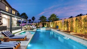 En swimmingpool med liggestole, en overdækket terrasse og en anlagt have.