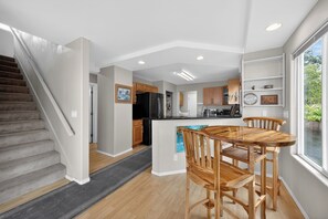 Eine moderne Küche mit Holzschränken, einem schwarzen Kühlschrank und einem Essbereich mit Holztisch und Stühlen.