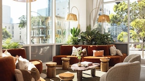 A modern lounge area with a sofa, chairs, a coffee table, and large windows offering a city view. - Ancora by Avantstay Bay Views + Rooftop Pool Heart of Little Italy (San Diego)