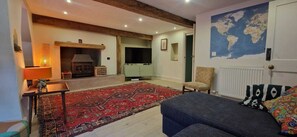 Ein gemütliches Wohnzimmer mit Kamin, Fernseher, großem Teppich und einem Bett mit gemusterten Kissen.