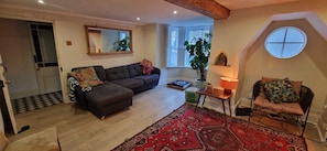 Ein Wohnzimmer mit einer Couch, einem kleinen Tisch mit Lampe, einem gemusterten Teppich und einem Sessel.