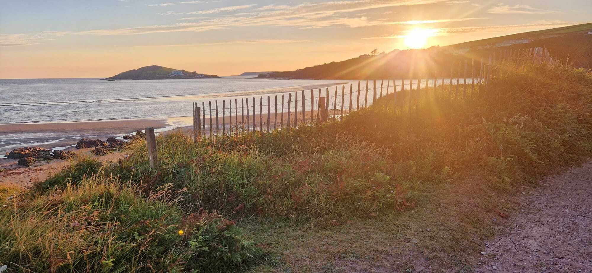 Un paysage côtier avec une clôture, une zone herbeuse et une étendue d’eau.