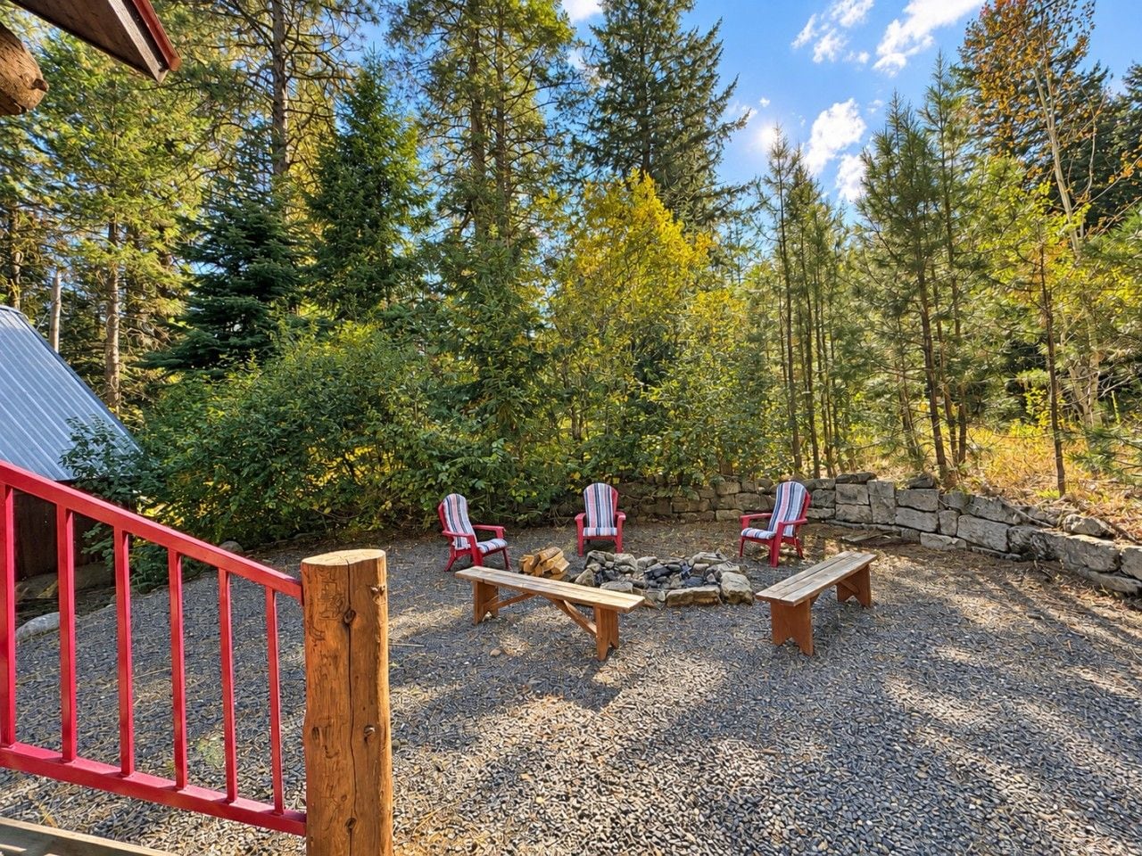 A wooden deck with Adirondack chairs, a fire pit, and a stone wall.