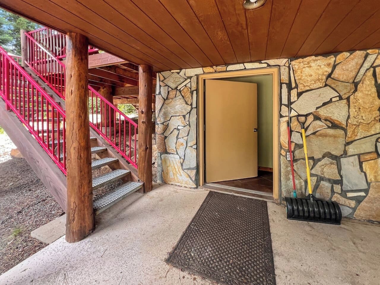 Una escalera de madera con barandales rojos que conduce a una entrada de pared de piedra.