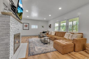 A modern living room with a fireplace, a sectional sofa, a coffee table, and a flat-screen TV mounted on the wall.