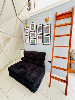 Um quarto com um sofá de cor escura, uma escada de madeira e uma parede decorada com quadros.