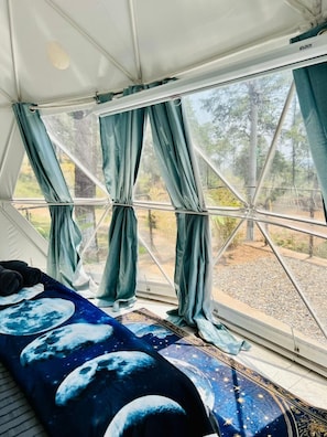 Um quarto com tenda, cama, cortinas e vista para as árvores.