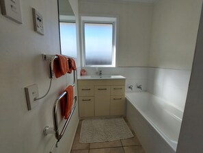 Un baño con bañera, lavabo, ventana y perchero para toallas.