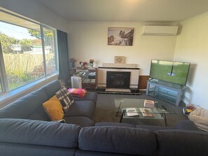 Una sala de estar con un sofá, una mesa de centro de vidrio, una chimenea, un televisor y vistas al exterior.