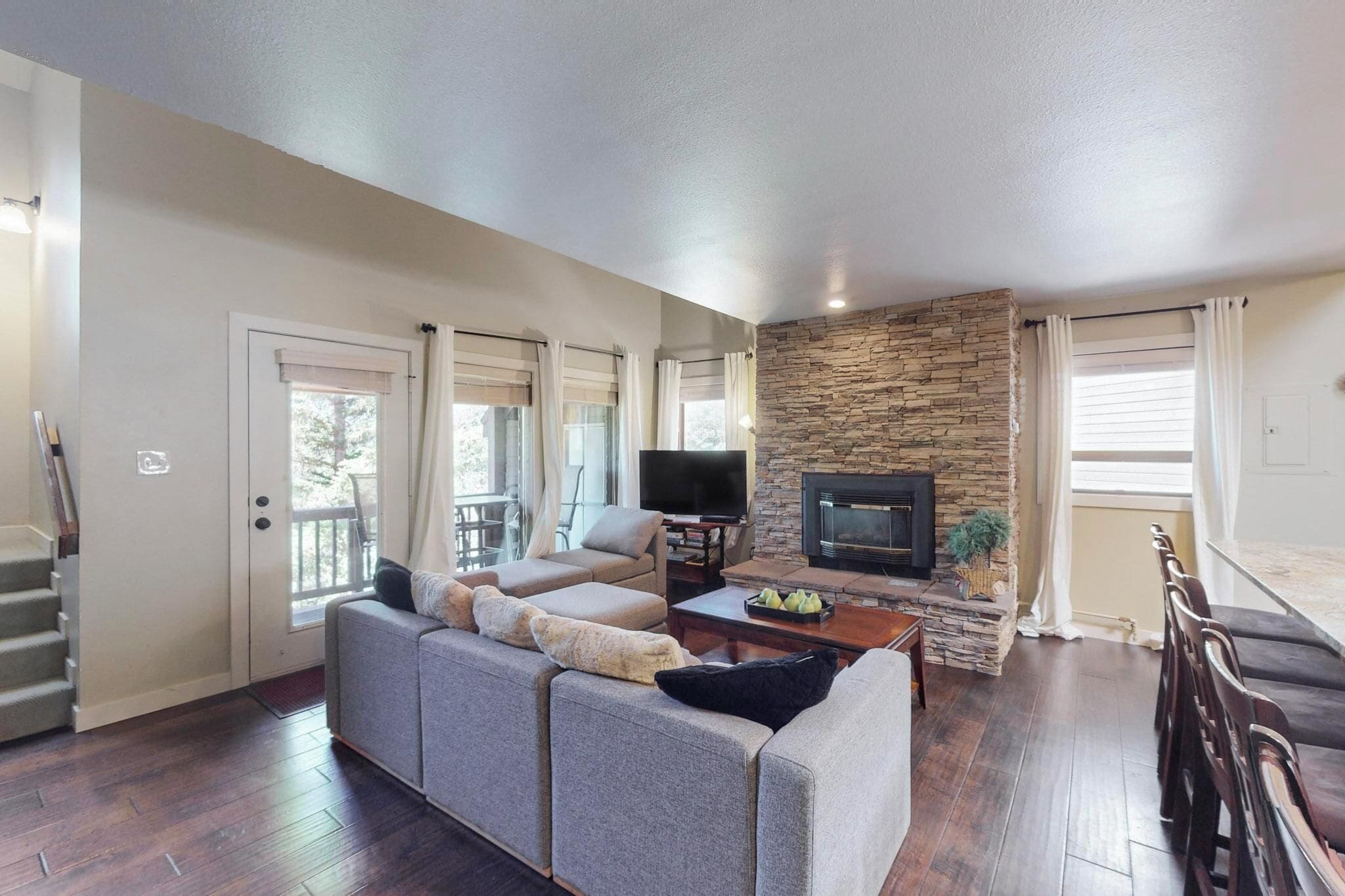 A living room with a stone fireplace, a sofa, a television, and a staircase.
