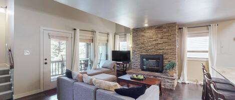A living room with a stone fireplace, a sofa, a television, and a staircase.