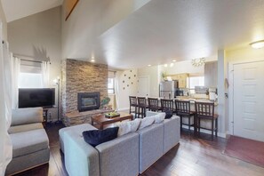 Ein Wohnzimmer mit Sofa, Fernseher, Kamin, Essbereich, Küche und einer Wand aus Stein.