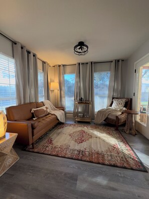 A living room with a brown sofa, a wooden chair, a patterned rug, and a chandelier. - Cozy Getaway, Close to Lake, Hot Tub (Lago Vista)
