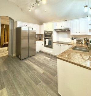 A modern kitchen with white cabinets, stainless steel appliances, granite countertops, and a wooden floor. - Cozy Getaway, Close to Lake, Hot Tub (Lago Vista)