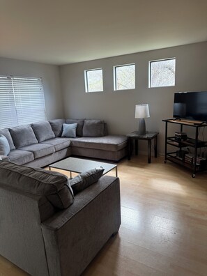 A living room with a sectional sofa, a coffee table, a TV on a stand, and a lamp.