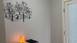 Quarto com um armário de madeira, um adorno de árvore na parede, uma luminária de sal e uma porta com persianas.
