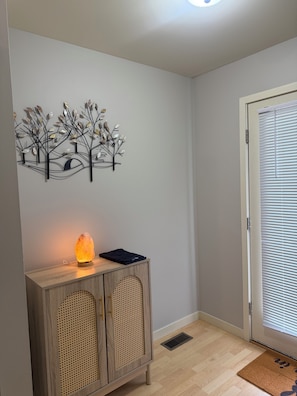 A room with a wooden cabinet, a wall-mounted tree decoration, a salt lamp, and a door with blinds.