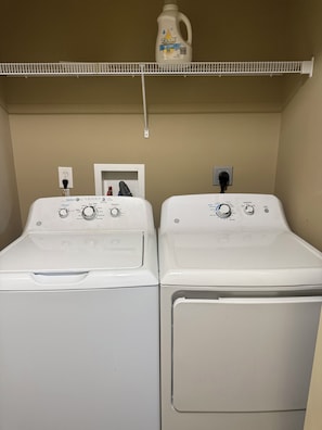 Two front-loading washers with control panels, a power outlet, and a bottle of liquid detergent on a shelf above.