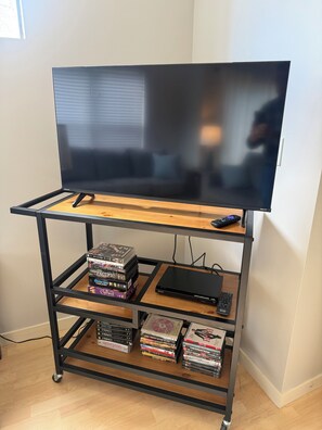 A TV on a wooden stand with a remote, a bookshelf with DVDs, and a gaming console.