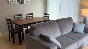 Sala de estar com sofá cinzento, mesa de jantar de madeira, cadeiras e luminária no teto.