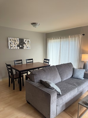 A living room with a grey sofa, wooden dining table, chairs, and a ceiling light fixture.