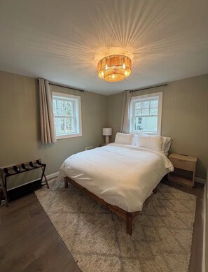 Ein Schlafzimmer mit einem Bett, zwei Nachttischen, einer Lampe, einer Bank und einer Deckenleuchte.