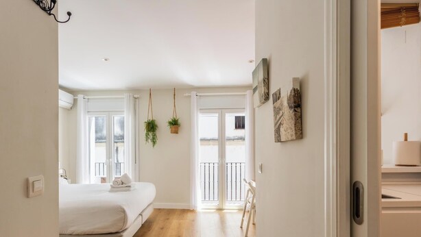 A bedroom with a bed, a window, a door, and a hallway leading to a bathroom. - Loft-style apartment in the El Pópulo district (Ciudad de Cádiz)
