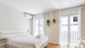 A bedroom with a bed, bedside table, hanging plants, and a balcony with a railing. - Loft-style apartment in the El Pópulo district (Ciudad de Cádiz)