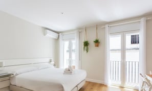 Ein Schlafzimmer mit Bett, Nachttisch, hängenden Pflanzen und einem Balkon mit Geländer.