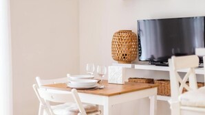 A dining area with a table set for two, a television on a shelf, and a wicker vase. - Loft-style apartment in the El Pópulo district (Ciudad de Cádiz)
