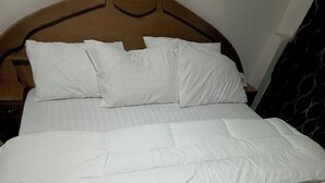 Uma cama grande com cabeceira de madeira, roupa de cama branca e piso de azulejos.