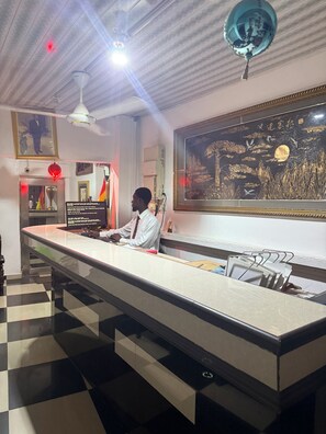 Un mostrador de recepción con una barra de registro, una obra de arte grande enmarcada en la pared y un ventilador de techo.