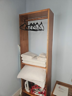 Un armario de madera con varios estantes, una barra para colgar ropa y una toalla doblada en el estante inferior.