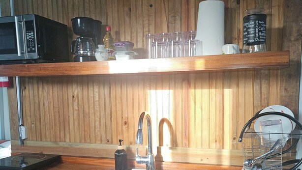 Keittiössä on puiset kaapit, ruostumattomasta teräksestä valmistettu pesuallas, mikroaaltouuni, kahvinkeitin ja hylly, jossa on lasiesineitä ja kahvinkeitin.